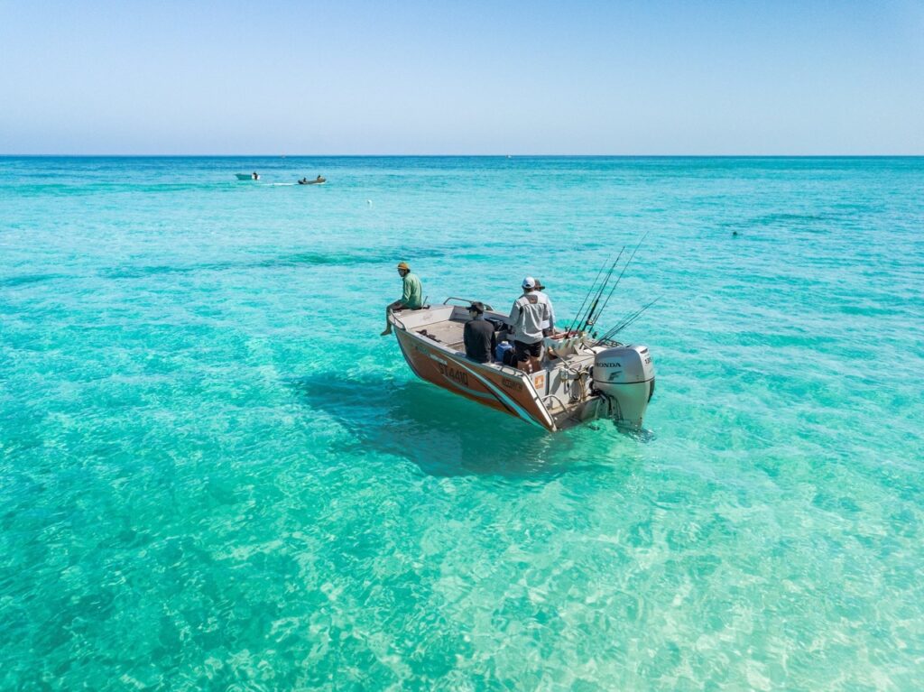 Two people on a motorboat fish in clear turquoise water under a bright blue sky.
