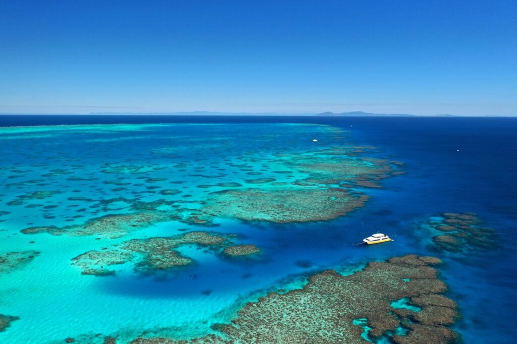 Aerial view of a boat near coral reefs in clear turquoise waters, under a cloudless blue sky.