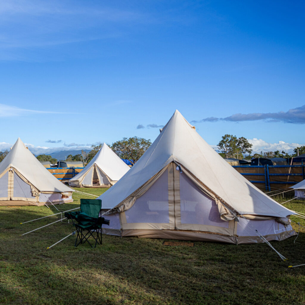 Several large canvas tents are set up on a grassy field under a clear blue sky, with folding chairs placed in front of one tent.