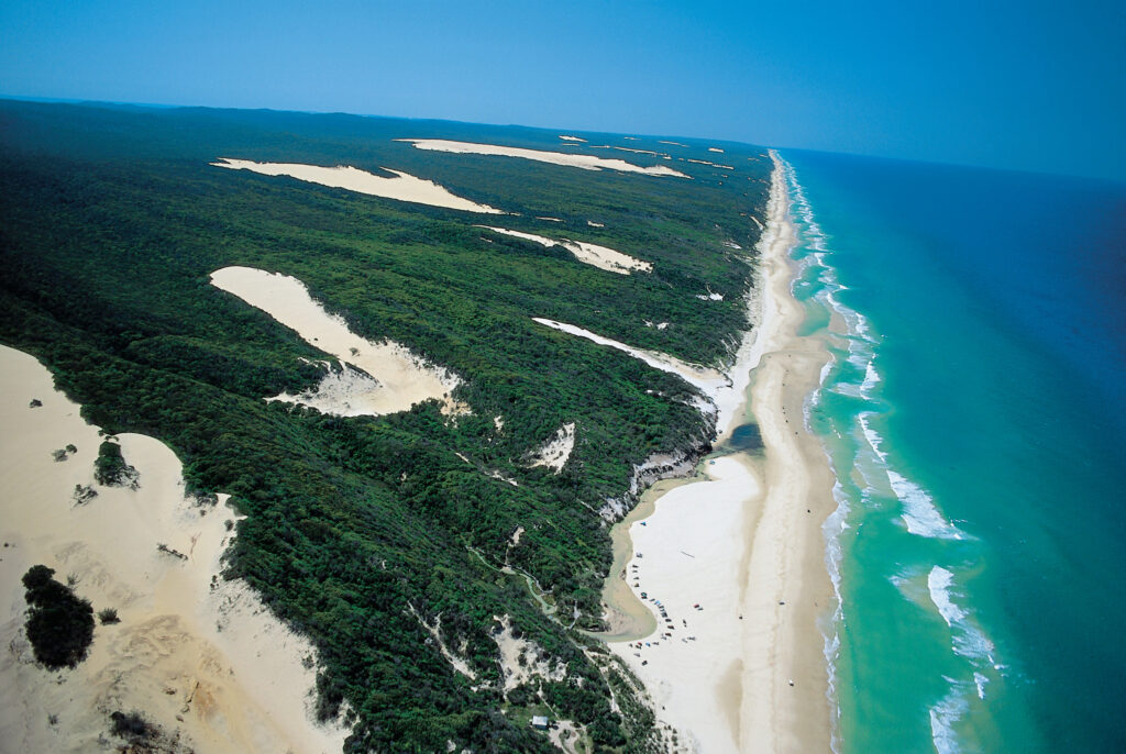 Aerial view of a coastline featuring sandy beaches, green vegetation, and turquoise ocean waters under a clear blue sky.