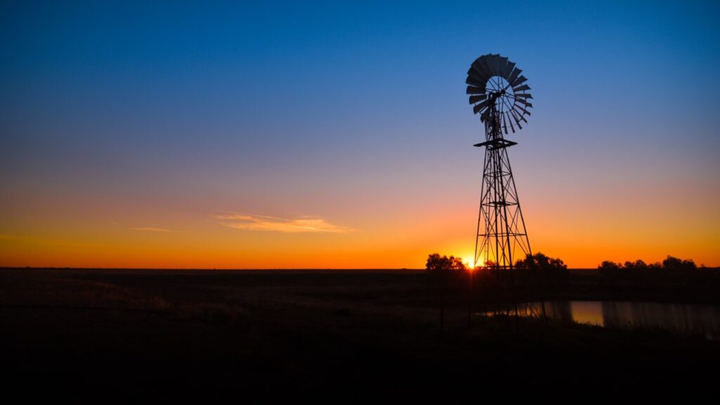 Windmill silhouetted against a vibrant sunset, with a clear sky and a faint cloud, over a flat landscape.