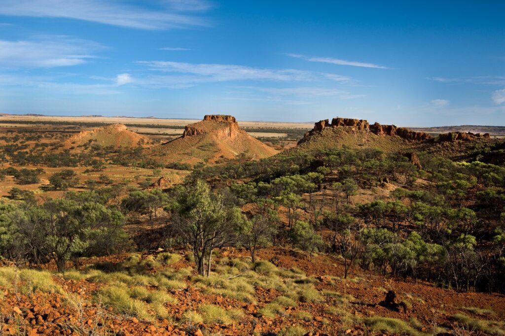 View of a vast desert landscape with rocky outcrops, sparse vegetation, and a clear blue sky.