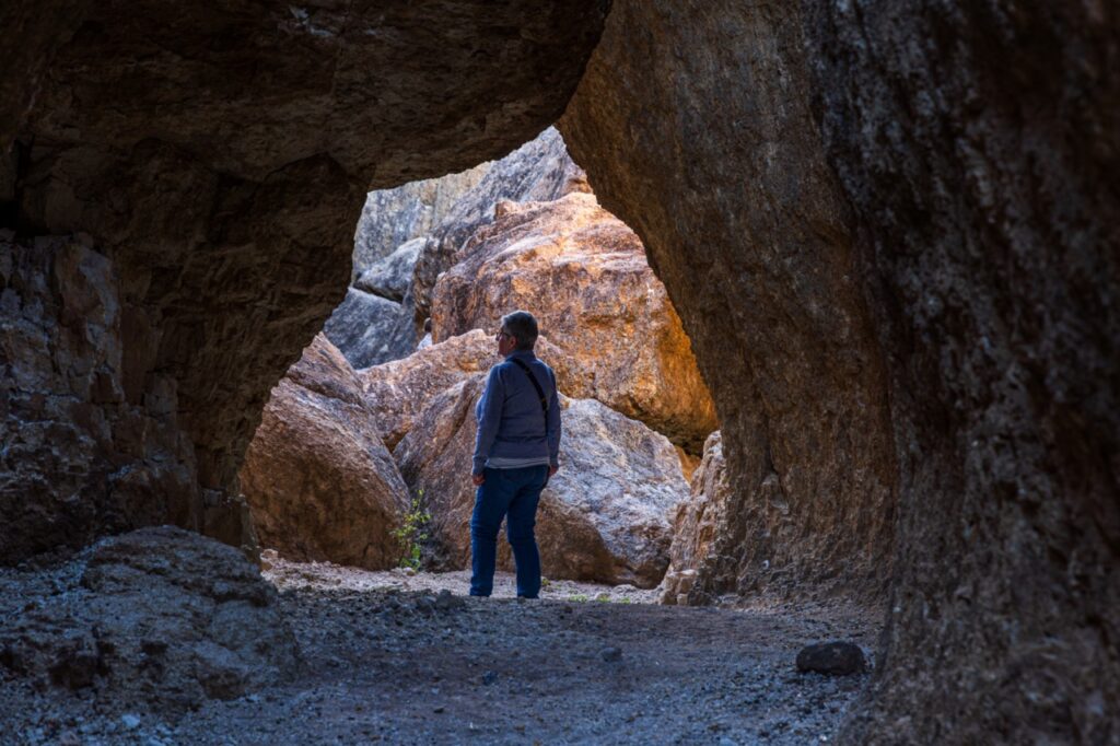 A person stands inside a rocky cave, looking at light coming through the entrance.