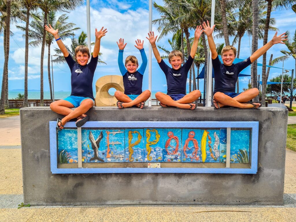 Four children in matching outfits sit on a wall with a 