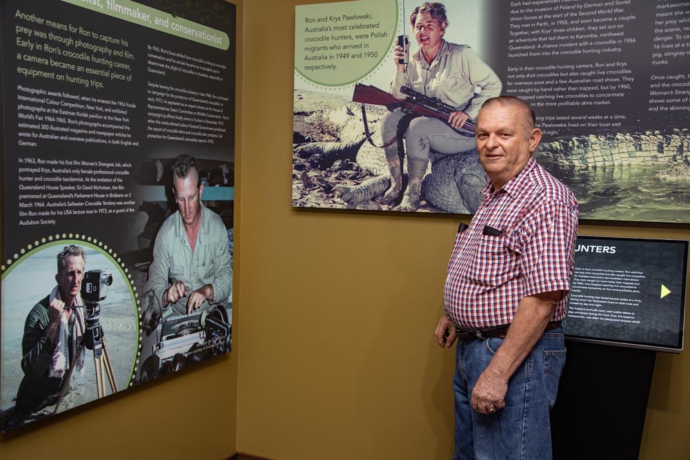 A man stands in a museum near display boards featuring information and images of a filmmaker and conservationist.