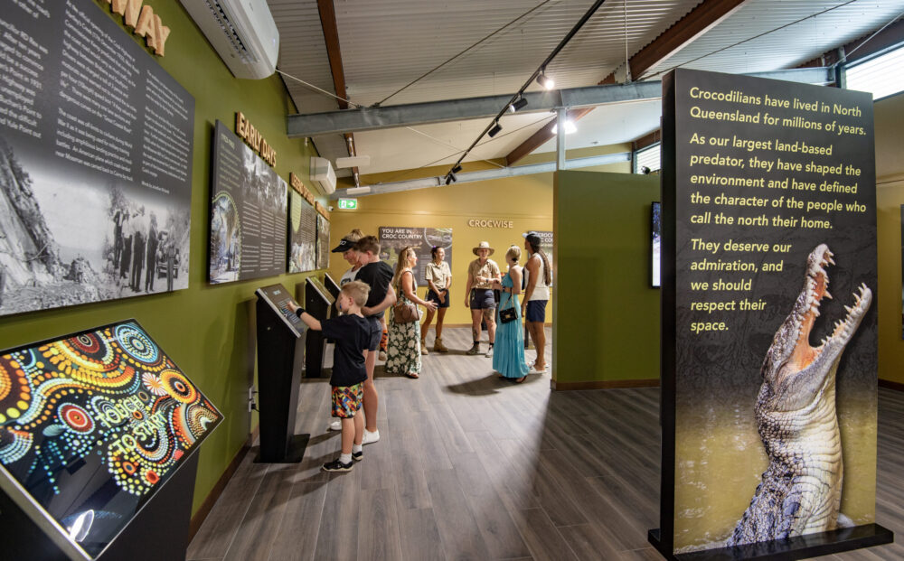 People explore an exhibit about crocodiles in Queensland, featuring interactive displays and informational panels.