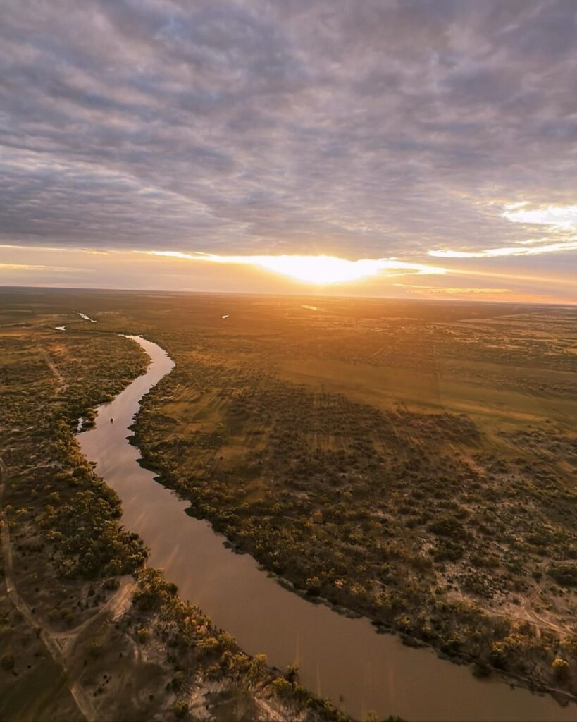 Aerial view of a winding river through a flat landscape at sunset, with a cloudy sky.
