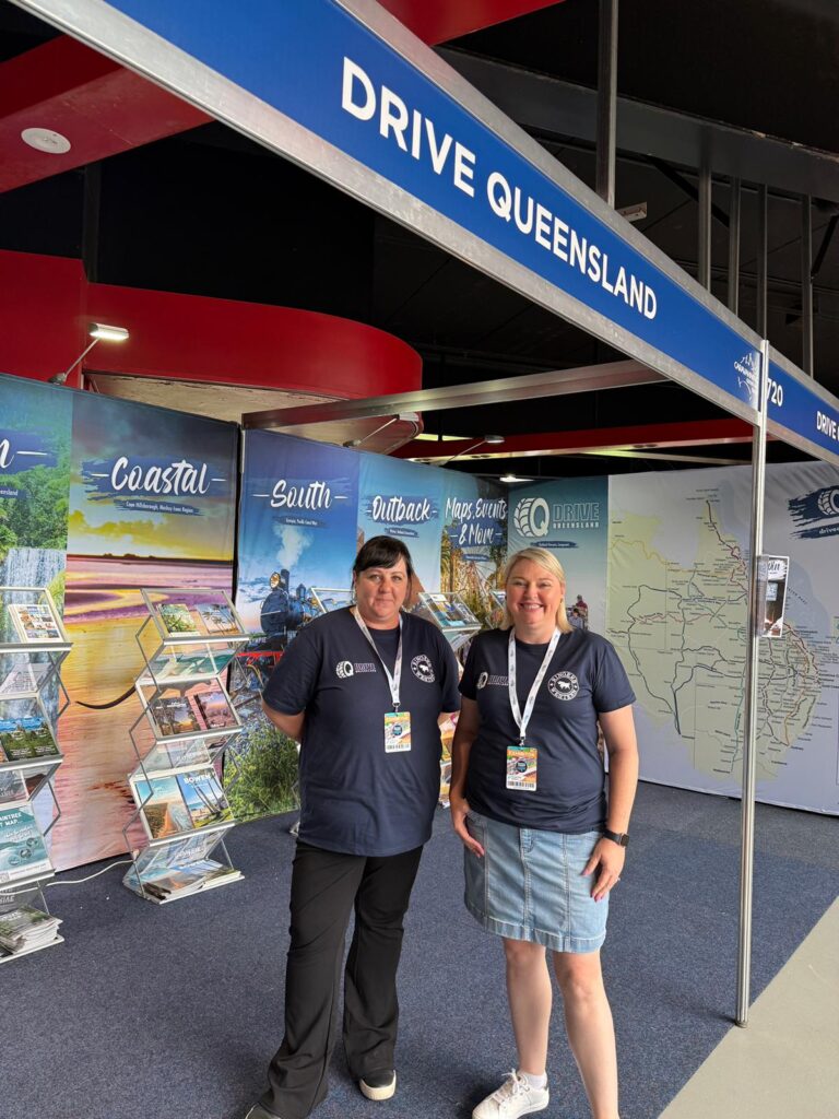 Two people wearing matching shirts and lanyards stand in front of a 