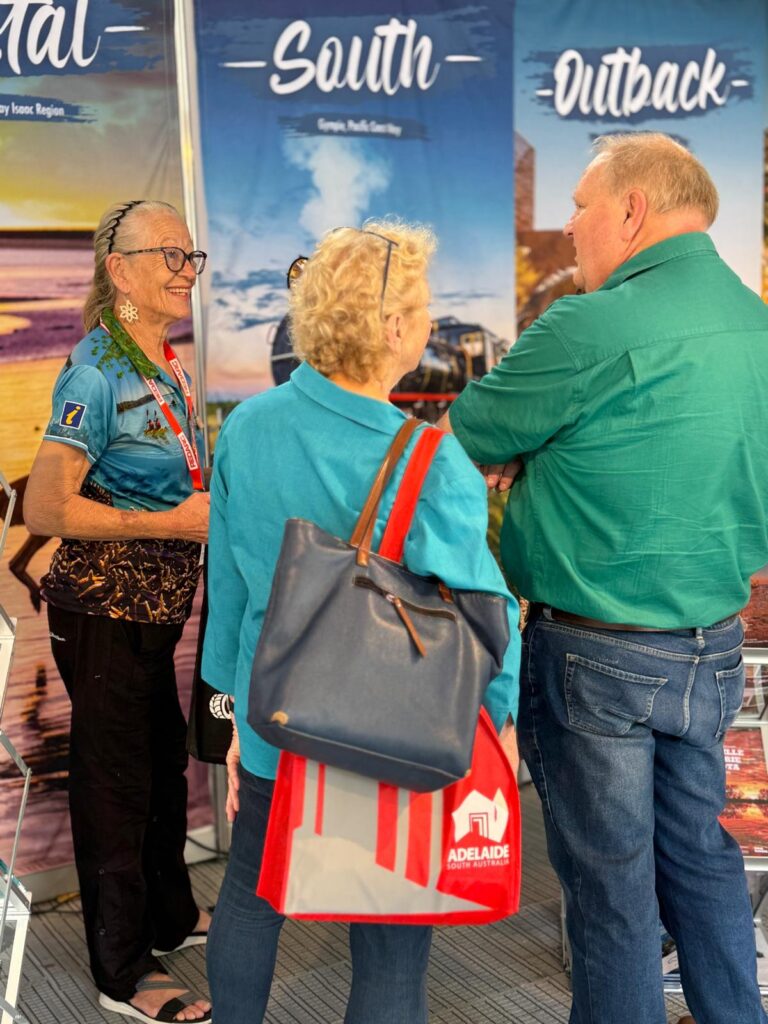 Three people stand and talk in front of travel posters labeled 