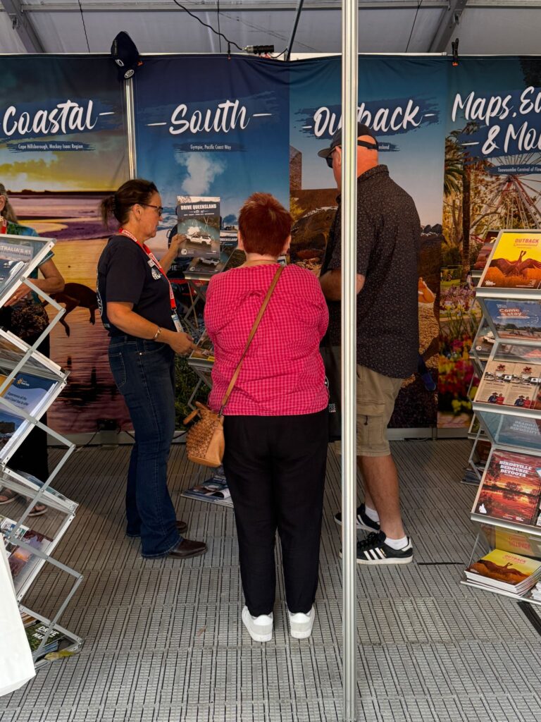 Three people stand inside a booth with travel brochures, large posters labeled 