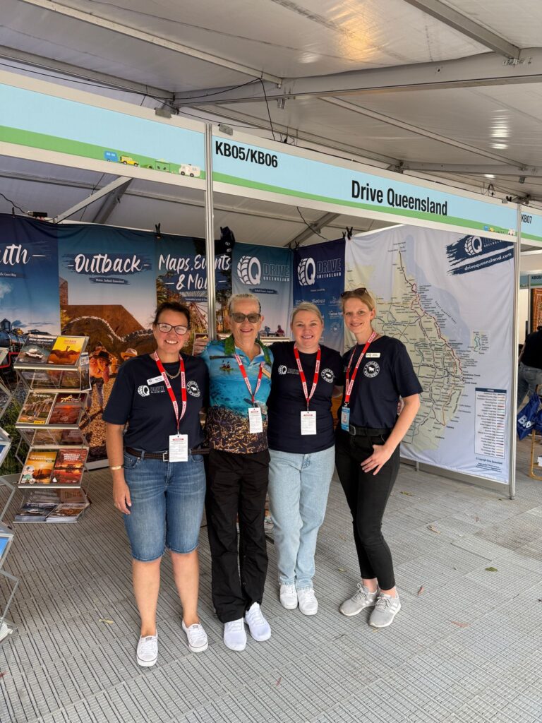 Four women wearing name badges and matching shirts stand in front of a 