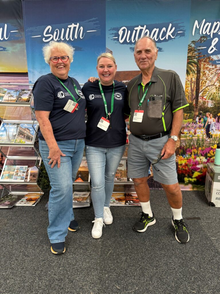 Three people stand smiling in front of a booth with travel brochures and banners reading 