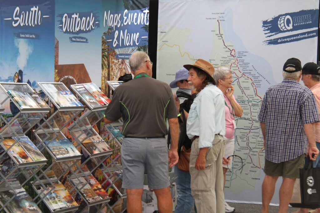 A group of older adults stands beside brochure racks and a large map display at a tourism information booth.