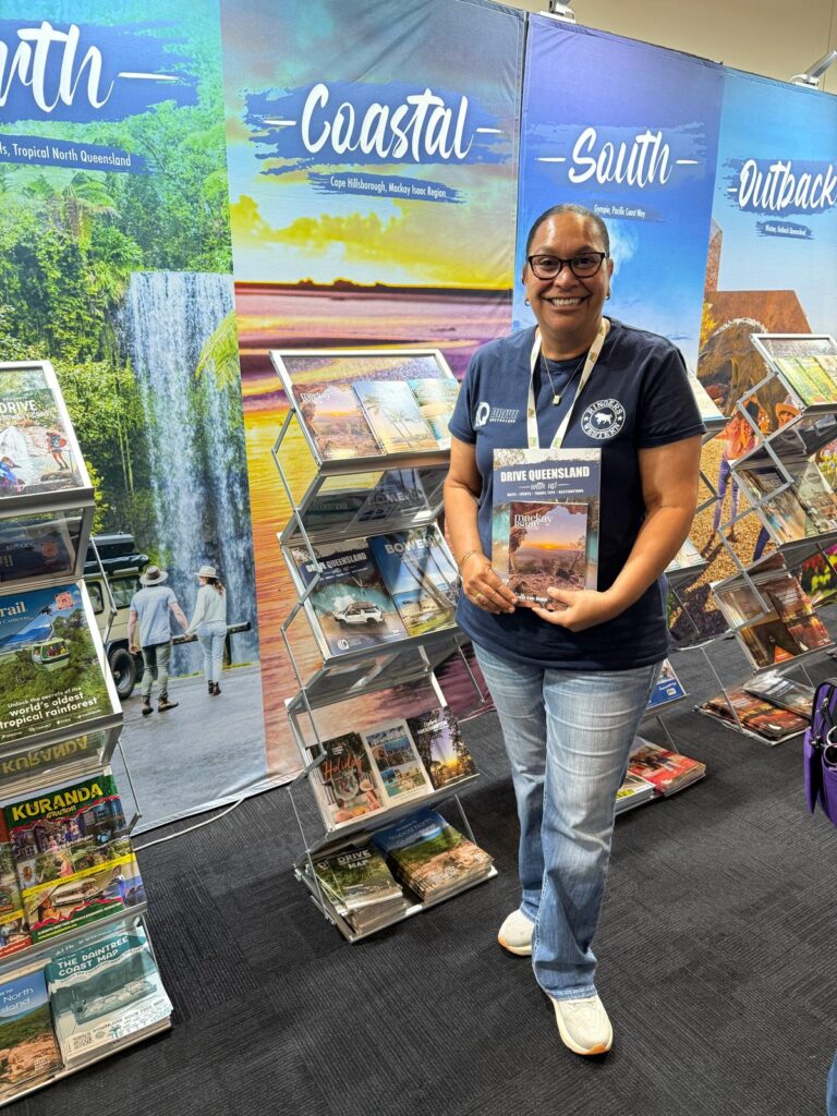 A woman in a navy shirt and glasses stands indoors holding a 