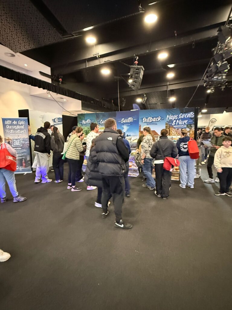 People stand in line indoors at a merchandise booth with banners and displays; most are wearing jackets and casual clothing.