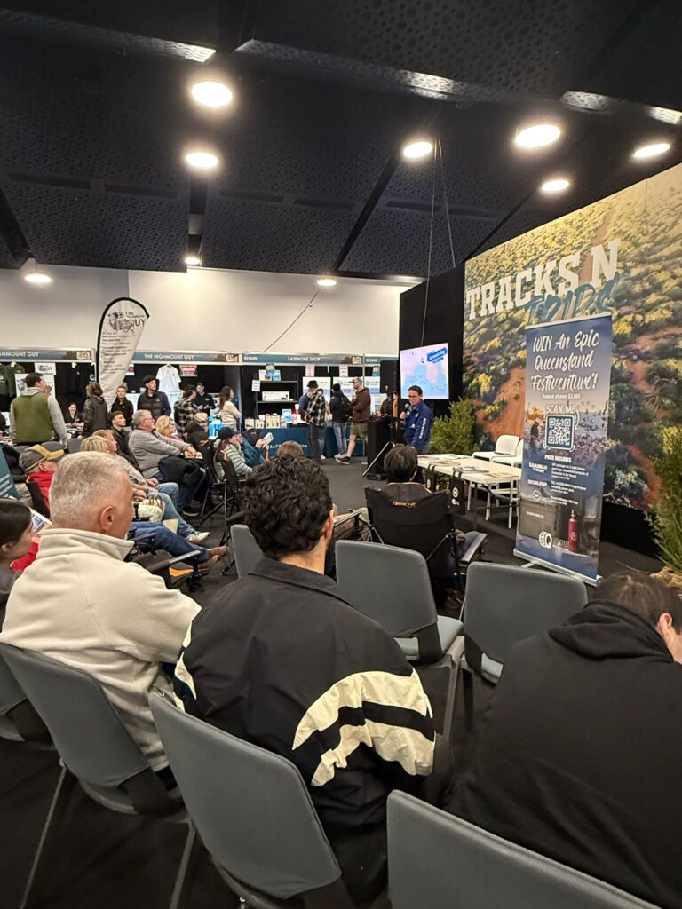 Audience seated at an indoor event with a stage, banners, and 