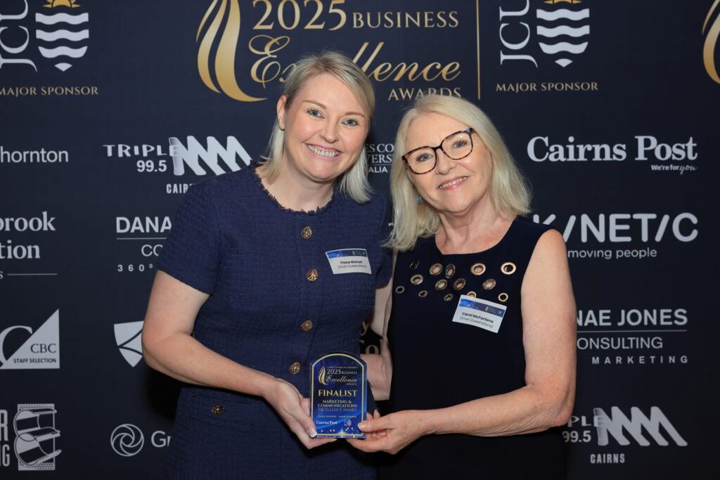 Two women smiling, holding a finalist award plaque at the 2025 Business Excellence Awards, standing in front of a sponsor backdrop.