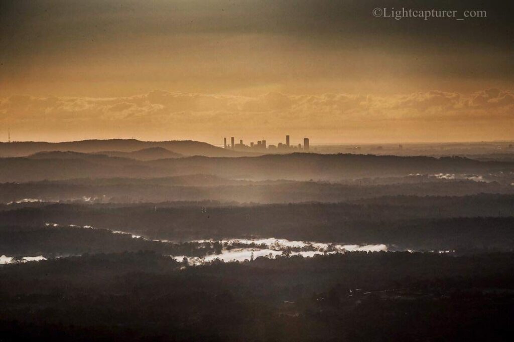 City skyline in the distance with layered hills and misty landscape in the foreground under a golden sky.