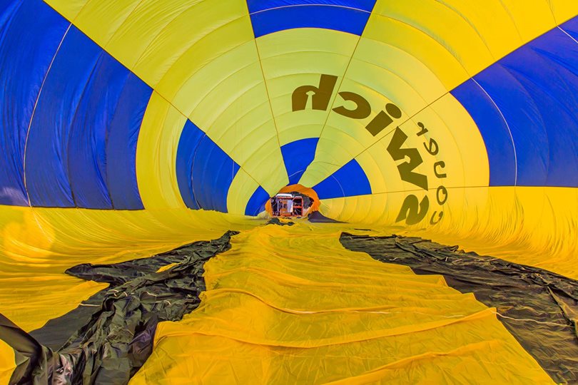 View from inside an inflated yellow and blue hot air balloon lying on the ground, with the basket visible at the far end.