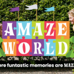 Two children peer at each other through a hedge maze. Colorful puzzle piece sign reads “Amaze World.” Text below says, “Where funtastic memories are MAZED!”.