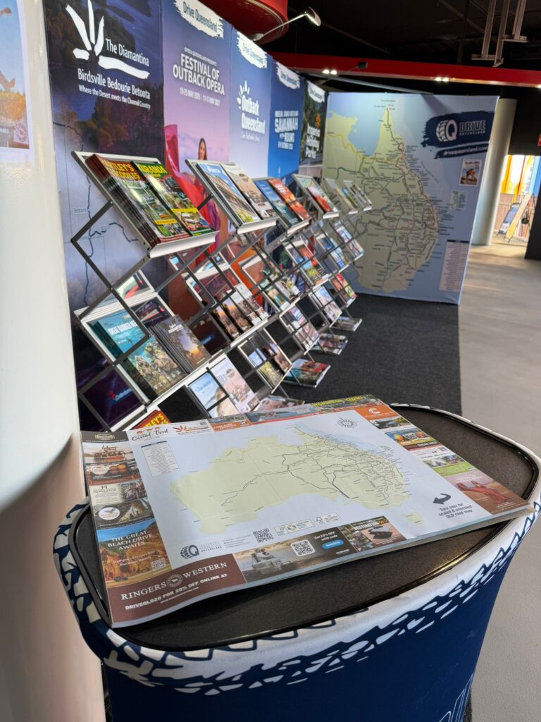 A display stand with brochures and maps about local attractions and events, with large wall maps and posters in the background.