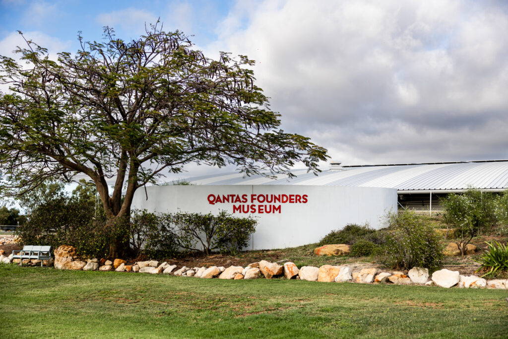 Exterior view of the Qantas Founders Museum building with a tree, greenery, and a stone border in the foreground.