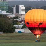 A hot air balloon with kangaroo silhouettes is grounded on a grassy field with city buildings and trees in the background.