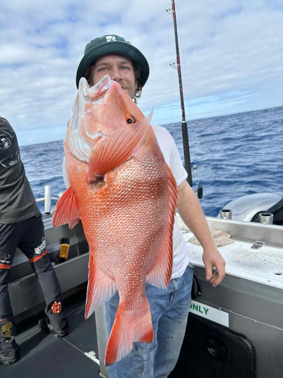 Person on a boat holding a large red fish with the ocean and fishing gear visible in the background.