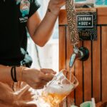 A person pours beer from a tap labeled "Jarrah Boy" into a glass mug at an outdoor setting.