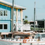 A white sailboat docked near a blue building displays a "Saltwater Eco Tours" banner on its side.