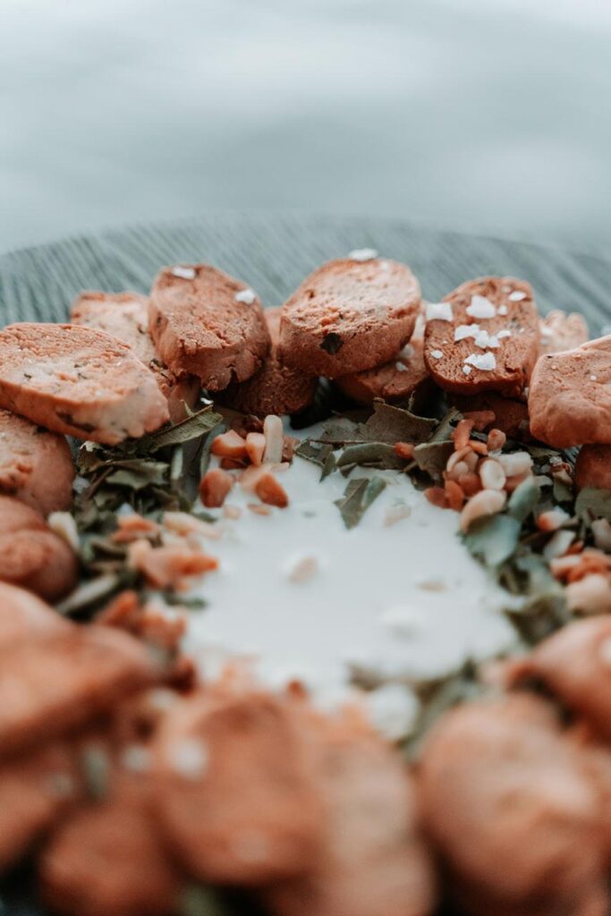 A plate with slices of biscotti arranged in a circle around a pool of white liquid, garnished with seeds and coarse salt.