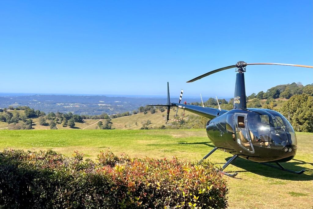 A black helicopter is parked on a grassy field with rolling hills and a clear blue sky in the background.