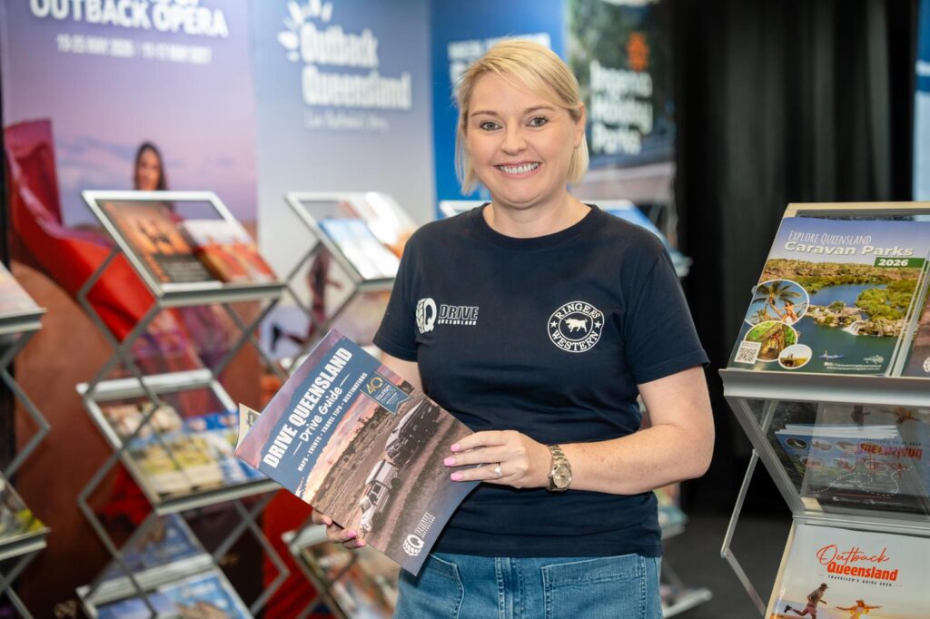 A woman stands in front of brochure racks, holding a 
