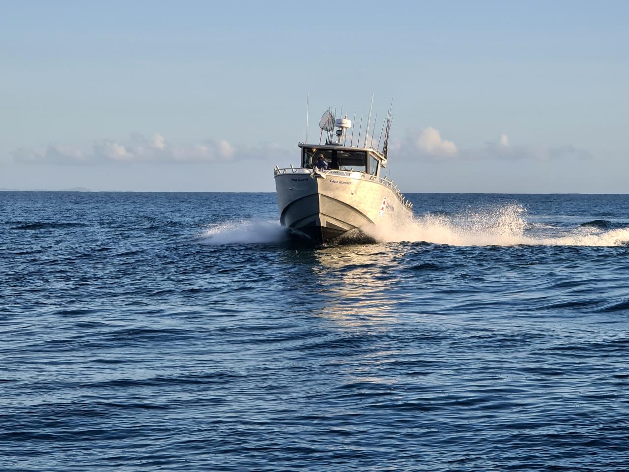 A white motorboat moves quickly across blue open water, creating waves and white spray behind it under a clear sky.