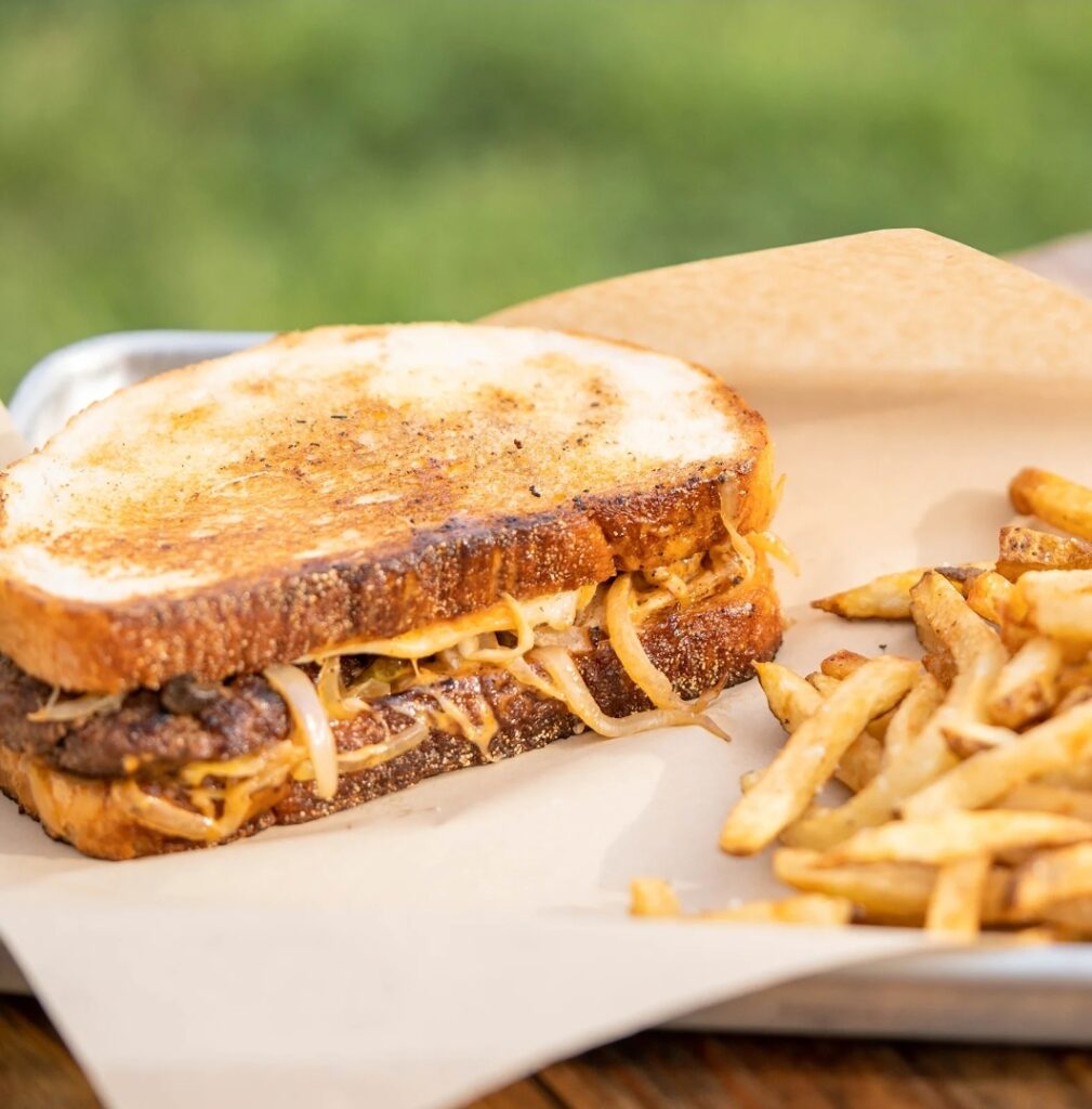 A grilled sandwich filled with melted cheese and onions is served on parchment paper next to a pile of French fries.