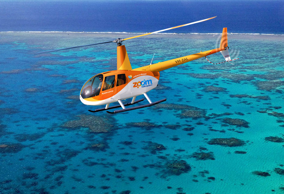 An orange and white Zoom Helicopters chopper flies over clear blue water and coral reefs.
